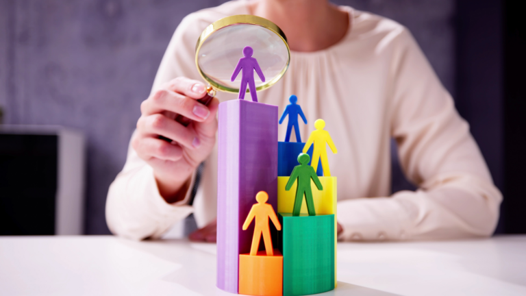 A woman holding a magnifying glass and looking closely at some human figurines